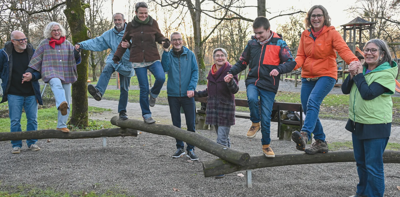 Mitglieder des Wohnprojekts balancieren lachend Hand in Hand über Baumstämme